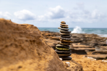 Fototapeta na wymiar Piles of stones built by child, standing on rocky sandy beach coast during spring summer day in Paphos, Cyprus