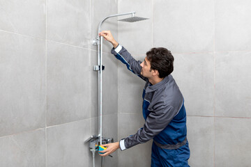 Handsome plumber fixing shower in the bathroom. Cheerful repairman standing and holding screwdriver in maintenance and service concept - obrazy, fototapety, plakaty