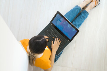 Top view of a young woman holding laptop computer on her lap while sitting at home