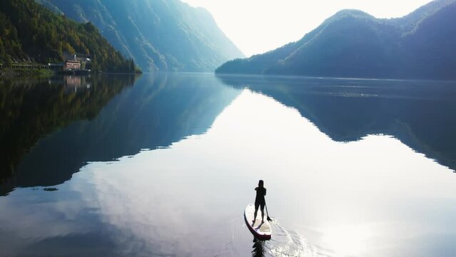 Tranquil and scenic drone shot of female traveller on paddle board on amazing norwegian fjord. Incredible cinematic scandinavian adventure. Drone shot of paddle board in Norway fjord