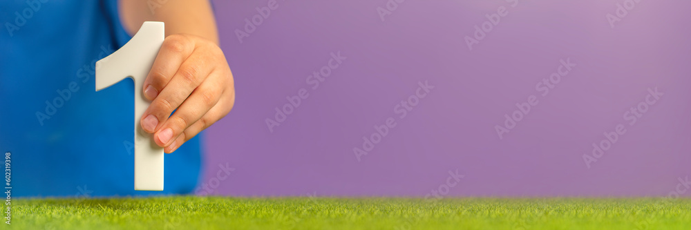 Aufkleber banner with hand holding number one on green grass and purple background. a symbol of unity, uniquen