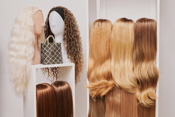 Showcase of natural looking wigs on female mannequin heads in beauty salon, hair on shelf in wig shop
