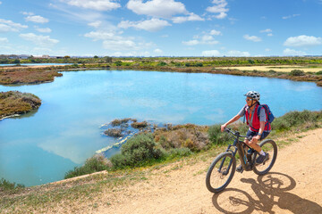 Fototapeta na wymiar beautiful senior woman cycling with her electric mountain bike on a via verde in the wetlands of Isla Christina, Andalusia, Spain