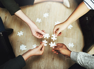 Hands, business people and puzzle in circle, huddle or teamwork for problem solving, solution or game in top view. Group, together and helping with support, synergy and team building on office floor