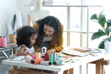 Dressmaker mom teaching her little daughter sewing, mother and daughter spend happily together