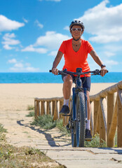 beautiful senior woman with her electric mountain bike at the golden sand beach of Isla Christina, Andalusia, Spain

