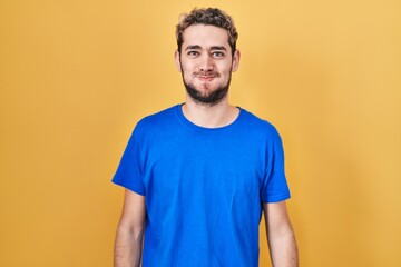 Fototapeta premium Hispanic man with beard standing over yellow background puffing cheeks with funny face. mouth inflated with air, crazy expression.