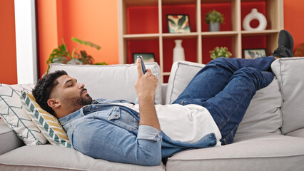 African american man using smartphone lying on sofa at home