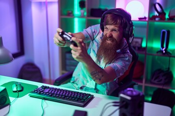 Fototapeta na wymiar Young redhead man streamer playing video game using smartphone at gaming room
