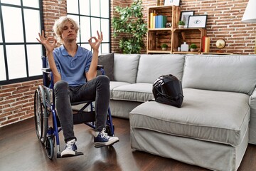 Young man sitting on wheelchair at for motorcycle accident relax and smiling with eyes closed doing meditation gesture with fingers. yoga concept.