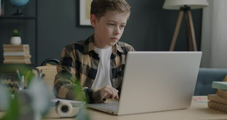 Portrait of pensive child working with laptop computer browsing sitting at desk at home. Modern lifestyle and happy childhood concept. - Powered by Adobe