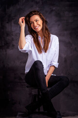 Studio portrait of a brunette haired attractive woman wearing white shirt and black jeans while posing at isolated dark background
