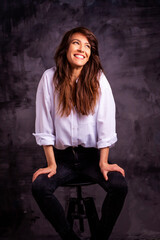 Fototapeta premium Studio portrait of a brunette haired attractive woman wearing white shirt and black jeans while posing at isolated dark background