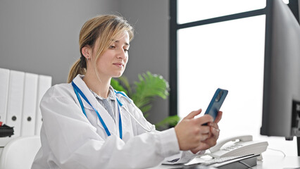 Young blonde woman doctor using smartphone working at clinic