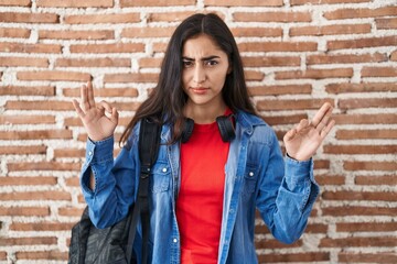 Young teenager girl wearing student backpack doing relax sign skeptic and nervous, frowning upset...