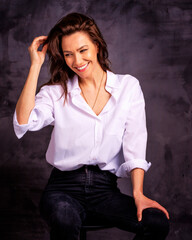 Fototapeta premium Studio portrait of a brunette haired attractive woman wearing white shirt and black jeans while posing at isolated dark background
