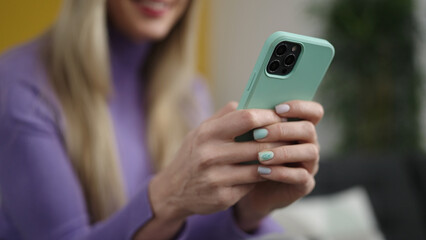 Young blonde woman using smartphone sitting on sofa at home