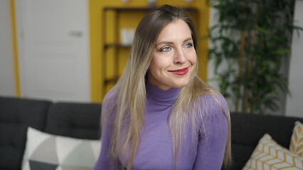 Young blonde woman smiling confident sitting on sofa at home