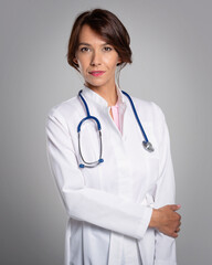 Female doctor wearing lab coat and stethoscope around her neck and standing at isolated background