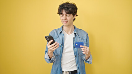 Young hispanic man shopping with smartphone and credit card over isolated yellow background