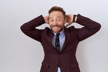 Middle age business man with beard wearing suit and tie relaxing and stretching, arms and hands behind head and neck smiling happy