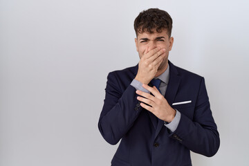 Young hispanic business man wearing suit and tie smelling something stinky and disgusting, intolerable smell, holding breath with fingers on nose. bad smell