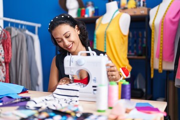 Young beautiful hispanic woman tailor smiling confident using sewing machine at clothing factory