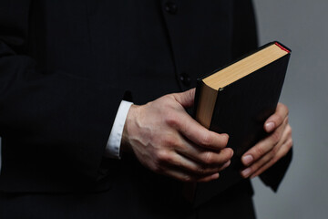 Close-up of pastor in black suit holding Bible book during sermon in church