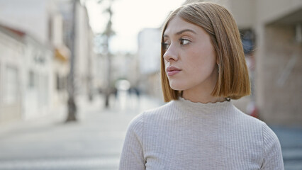 Young blonde woman looking to the side with serious expression at street