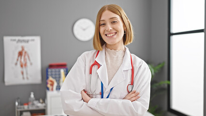 Young blonde woman doctor smiling confident standing with arms crossed gesture at clinic