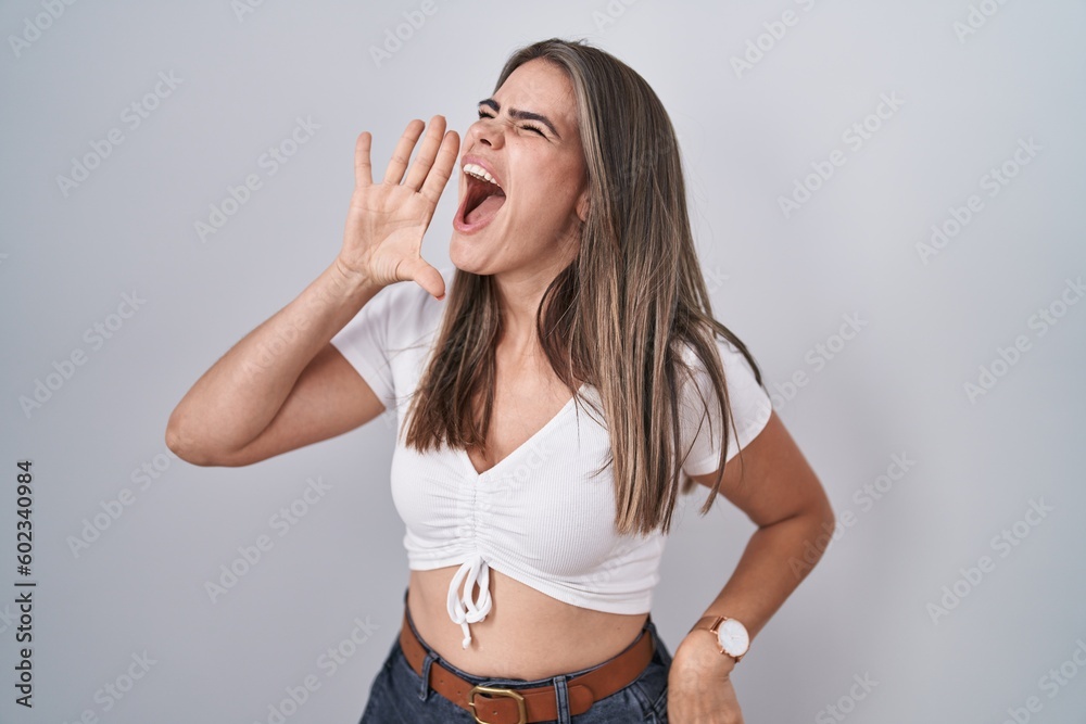 Wall mural Young beautiful woman wearing casual white t shirt shouting and screaming loud to side with hand on mouth. communication concept.