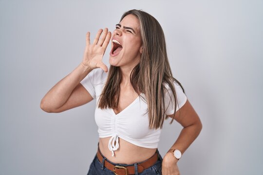 Young beautiful woman wearing casual white t shirt shouting and screaming loud to side with hand on mouth. communication concept.
