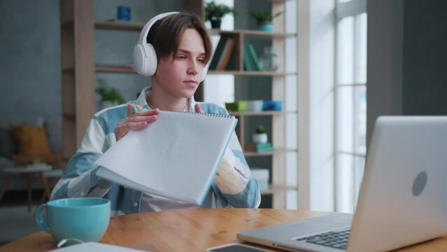 Young Boy Listening Music in Headphones and Writing in Notebook Looking at Display of Laptop Computer. Virtual E-learning of Teenage Student at Educational Pc on Desk. Pupil Watching Video Information