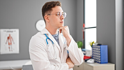 Young hispanic man doctor standing with doubt expression thinking at clinic