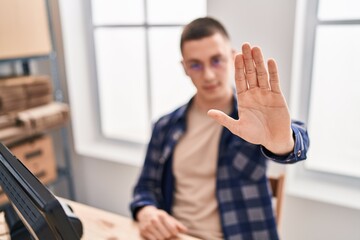 Young hispanic man ecommerce business worker doing stop gesture with hand at office