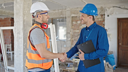 Two men builder and architect shake hands speaking at construction site