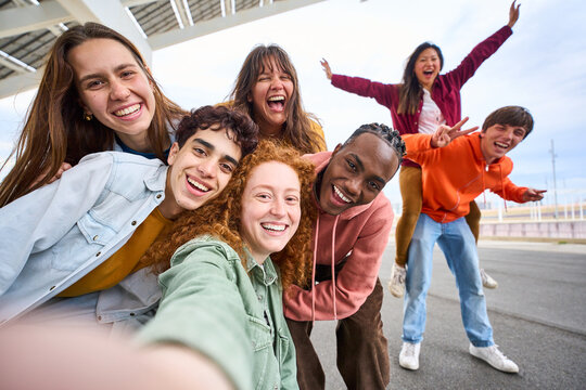 Group of happy multiracial friends taking a selfie photo with cell phone outside. Happy young people together smiling at camera. Youth concept with boys and girls having fun walking along city street.