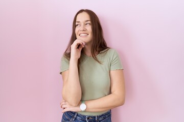 Beautiful brunette woman standing over pink background with hand on chin thinking about question, pensive expression. smiling and thoughtful face. doubt concept.