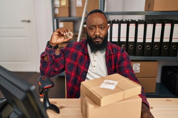 African american man working at small business ecommerce holding bitcoin thinking attitude and sober expression looking self confident