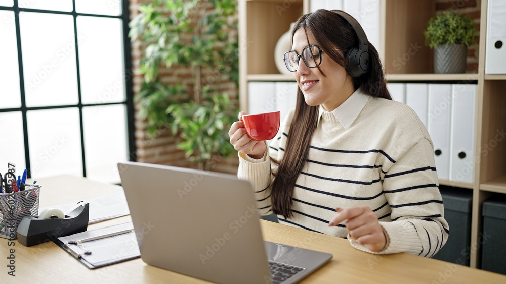 Poster Young beautiful hispanic woman business worker listening to music drinking coffee at office