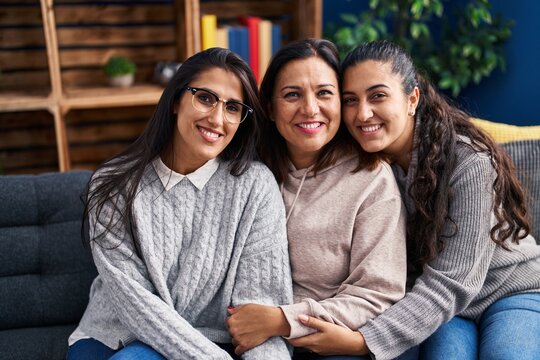 Three woman hugging each other sitting on sofa at home