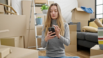 Young caucasian woman sitting on the floor using smartphone at new home