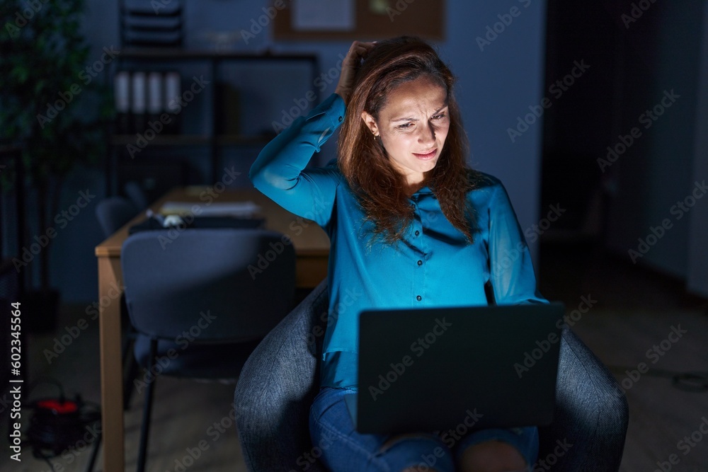 Wall mural Brunette woman working at the office at night confuse and wonder about question. uncertain with doubt, thinking with hand on head. pensive concept.