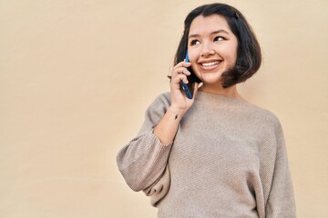 Young woman smiling confident talking on the smartphone over yellow background