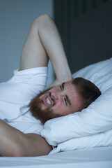 Young sad depressed unhappy worried man in the bed in bedroom at home in the morning lying under...