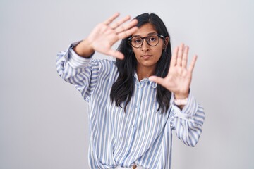 Young hispanic woman wearing glasses doing frame using hands palms and fingers, camera perspective