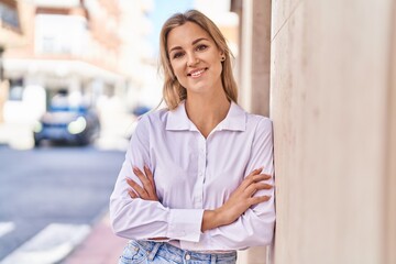 Fototapeta premium Young blonde woman smiling confident standing with arms crossed gesture at street