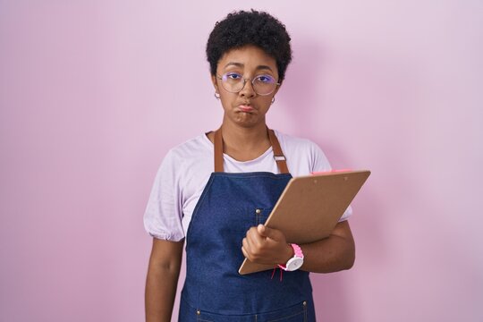 Young african american woman wearing professional waitress apron holding clipboard depressed and worry for distress, crying angry and afraid. sad expression.