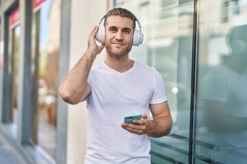 Young caucasian man listening to music standing at street