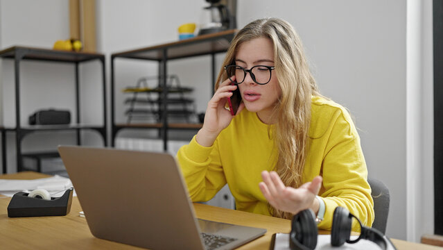 Young blonde woman business worker using laptop talking on smartphone at office